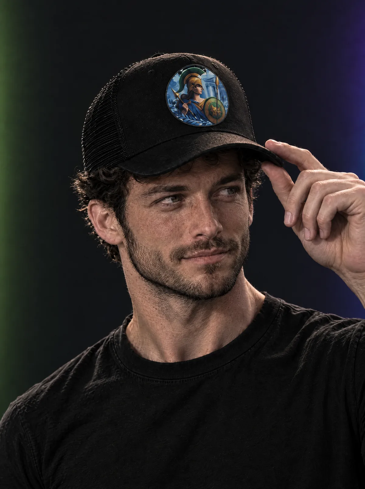 The same man touching the brim of a black trucker hat with a round Athena emblem